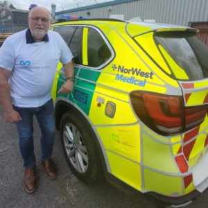 Alex Murphy Stands Next To One Of His Ambulance's In A Little LifeSavers T-shirt.