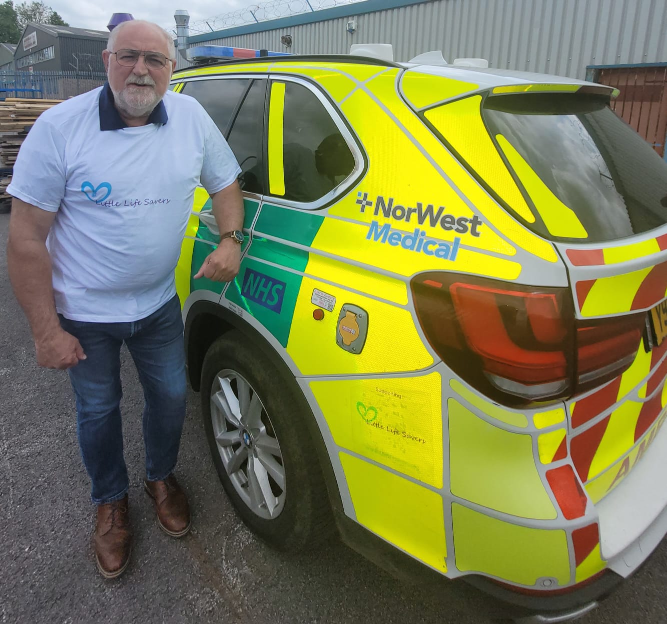 Alex Murphy Stands Next To One Of His Ambulance's In A Little LifeSavers T-shirt.